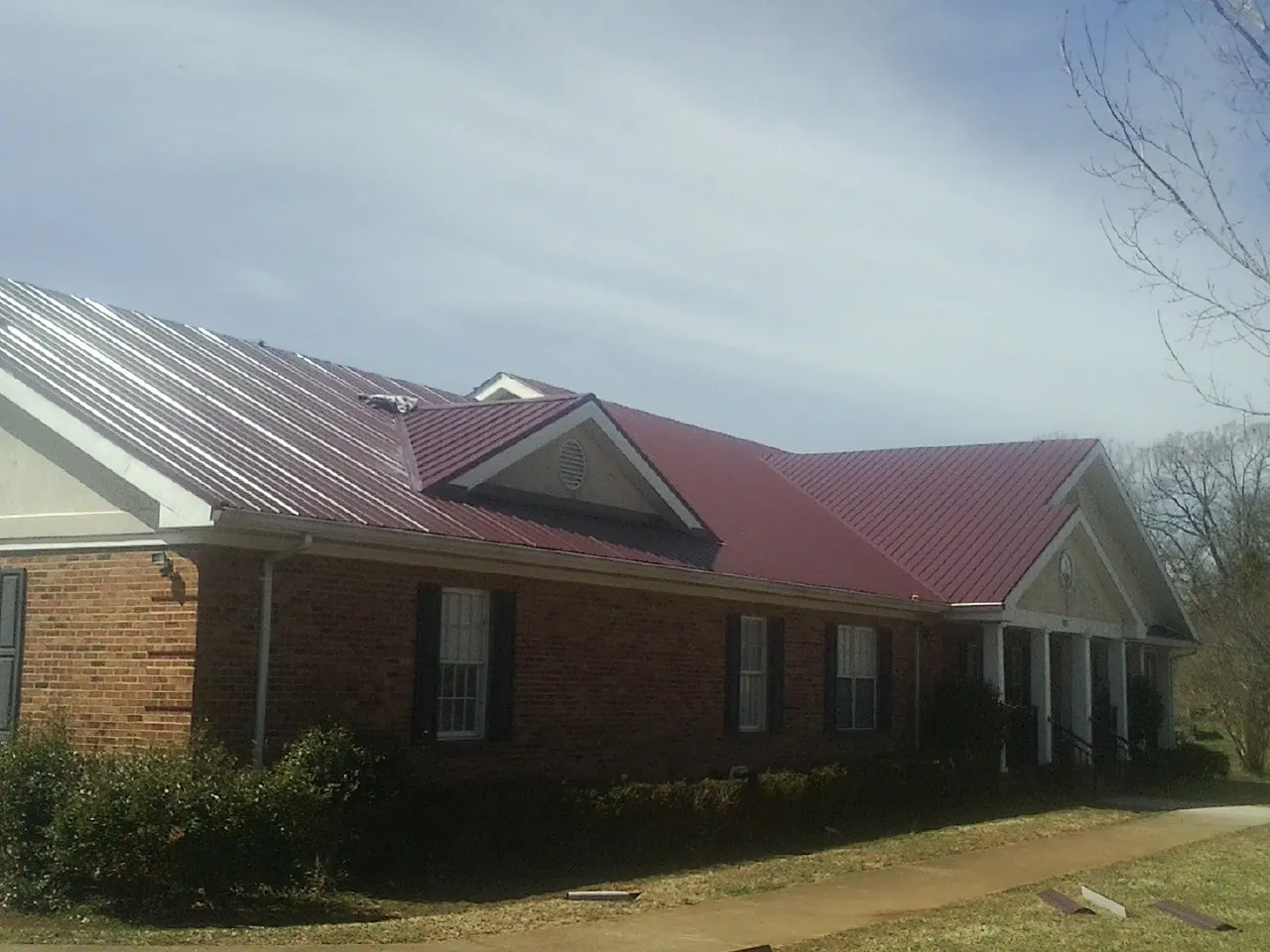 Red metal roof with gabled entries on a long brick building, from a Hail Damage Roof Repair job in Sutton