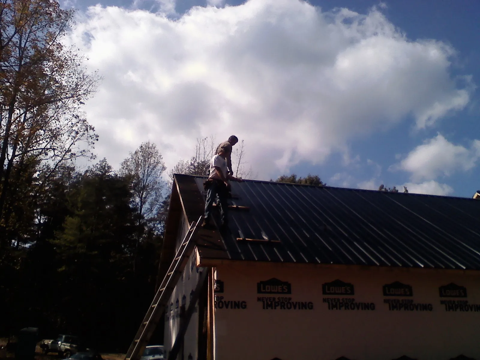 Roofer fastening dark metal panels high against a cloudy sky, from a Roof Inspection job in Sutton